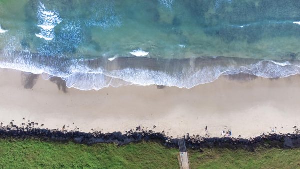 Aerial snap looking directly down on Seven Mile Beach in Lennox Head, showing one of the beach's entry sites as well as the nearby grass and rocks.
