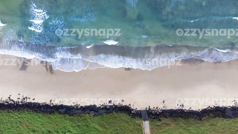 Straight-down aerial shot of Seven Mile Beach Aerial snap looking directly down on Seven Mile Beach in Lennox Head, showing one of the beach's entry sites as well as the nearby grass and rocks.