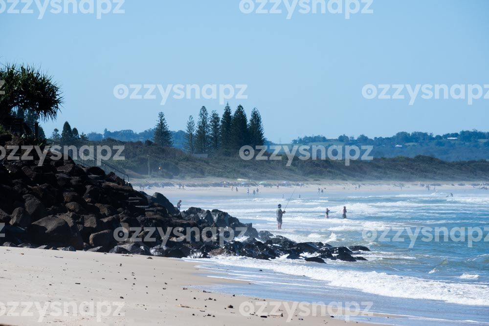 From Seven Mile Beach looking towards Lennox Head Beach Lennox Head Beach from Seven Mile Beach. With a backdrop of greenery, there are people fishing, swimming, and enjoying the beach.