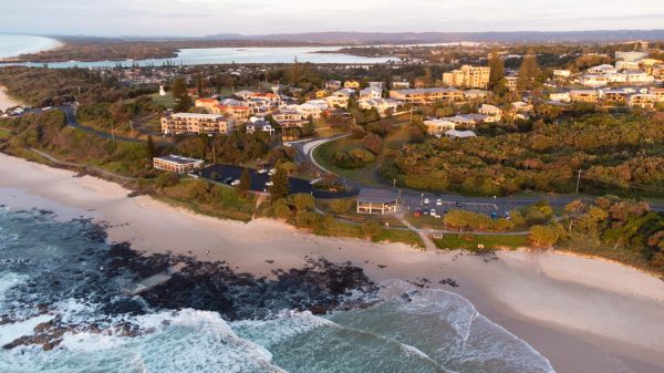 Stock image of Shelly Beach during sunrise, featuring the rockpool, beach-front houses and apartments, and lush greenery.
