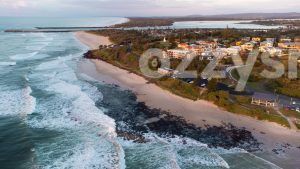 Stunning drone shot of Shelly Beach Sunrise, showcasing the beachfront houses and apartments, the Richmond River, and the Ballina Lighthouse.