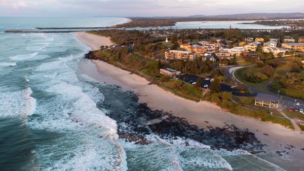 Stunning drone shot of Shelly Beach Sunrise, showcasing the beachfront houses and apartments, the Richmond River, and the Ballina Lighthouse.