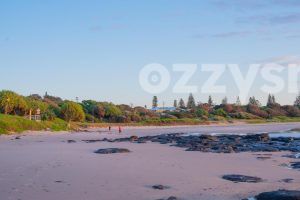 Shelly Beach during sunrise with two women walking among lush greenery and rocks.