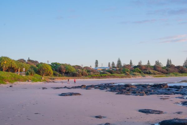 Shelly Beach during sunrise with two women walking among lush greenery and rocks.