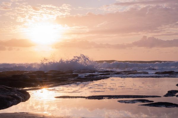 Stunning stock photo of Shelly Beach at sunrise, featuring waves crashing onto rocks and a serene rock pool reflecting the beautiful colors of the sky.