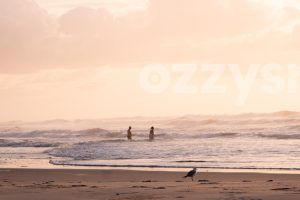 Serene image captures two people walking into the ocean during sunrise at Shelly Beach, East Ballina.