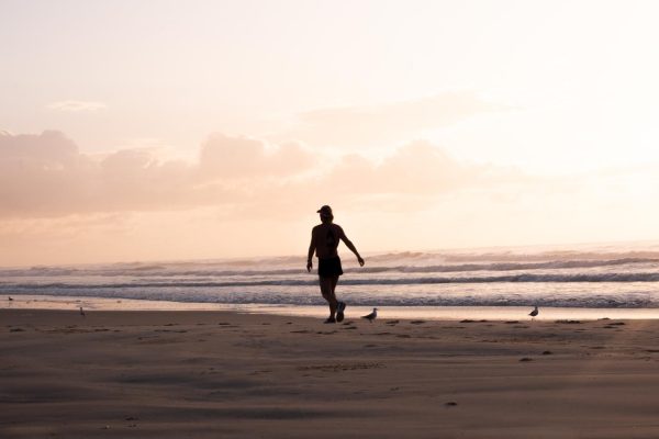 Serene stock image of a person jogging at Shelly Beach during sunrise. Waves, seagulls, and soft pink hues of the sky create a peaceful atmosphere.