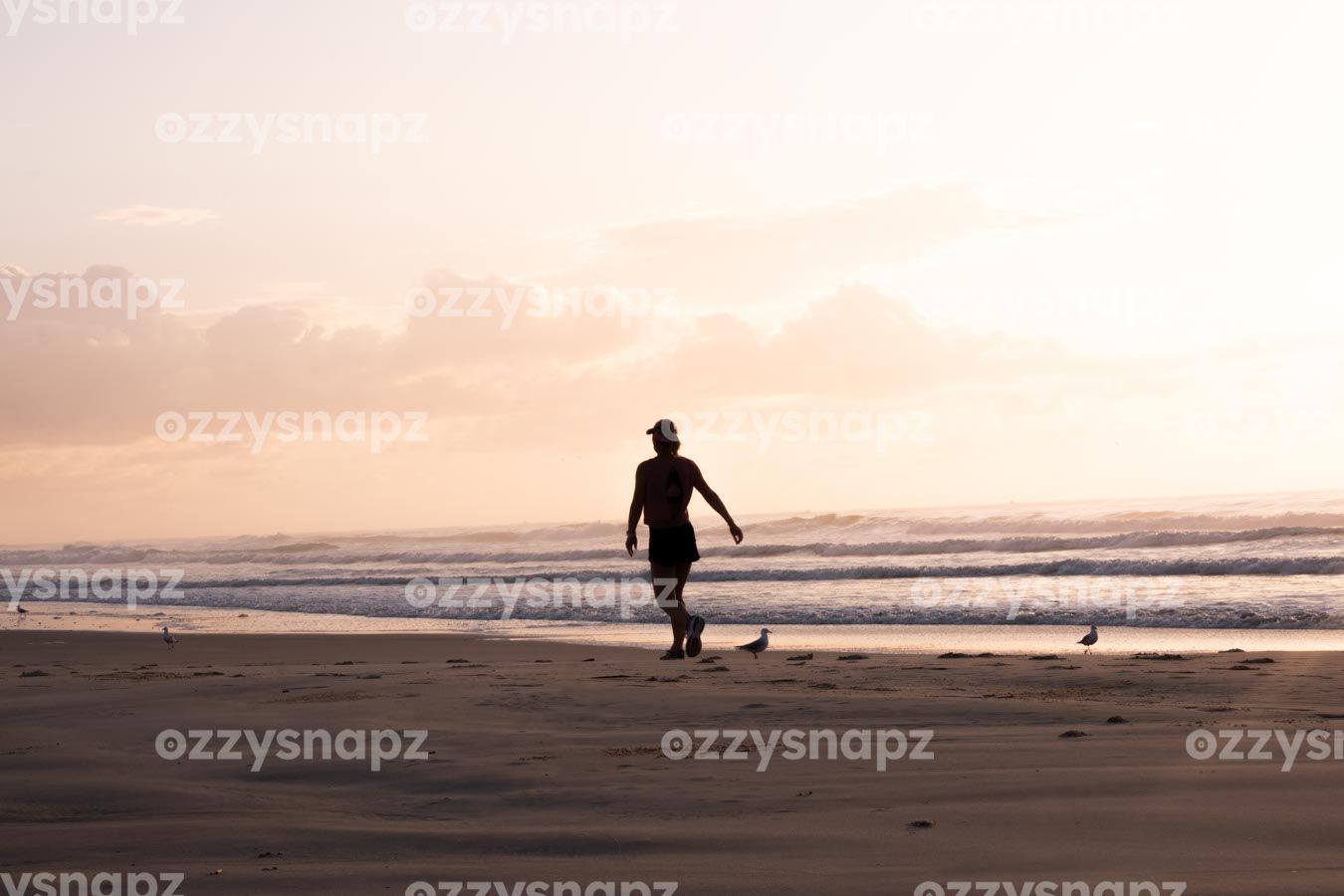 ozzysnapz_221353_low Serene stock image of a person jogging at Shelly Beach during sunrise. Waves, seagulls, and soft pink hues of the sky create a peaceful atmosphere.