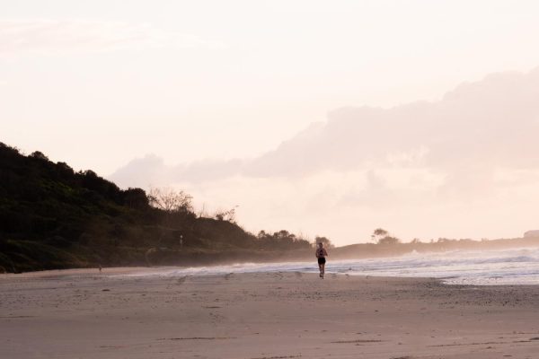Serene digital stock image of a person jogging on Shelly Beach at sunrise with beautiful bushland in the background.