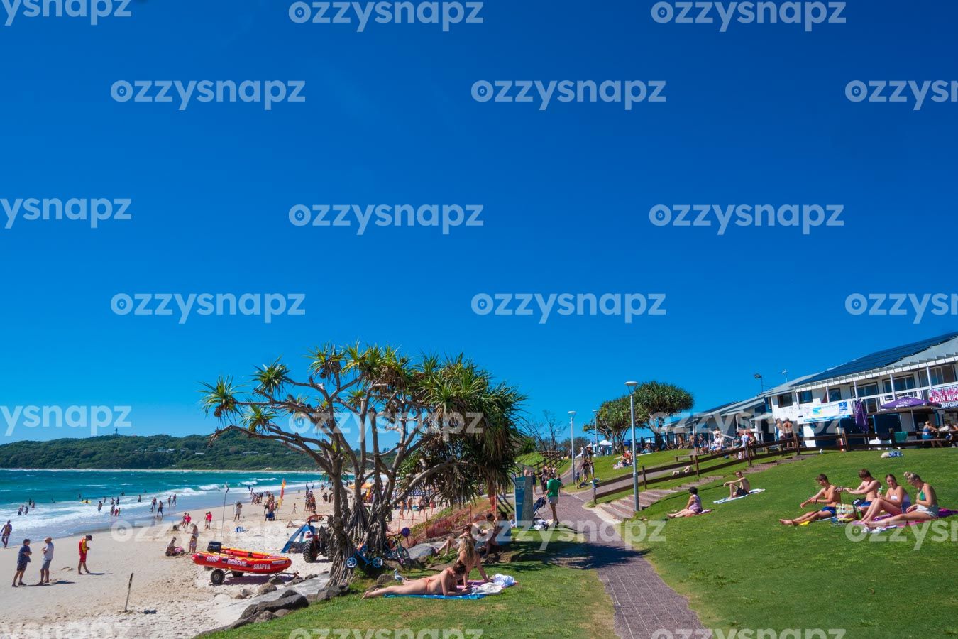 ozzysnapz_221413_low Byron Bay Main Beach and Apex Park, with sunbathers, surf life saving club, and the iconic lighthouse in the background.